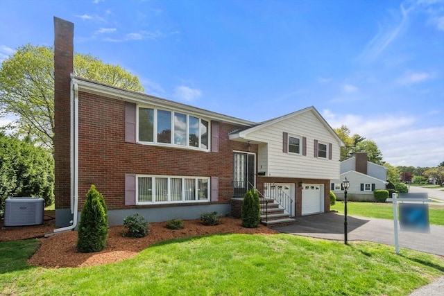 bi-level home with central AC unit, driveway, a garage, a front lawn, and brick siding