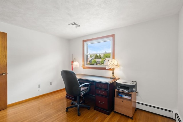 office space with a baseboard heating unit, light wood finished floors, baseboards, and a textured ceiling