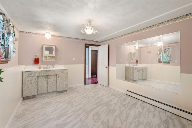 empty room featuring baseboard heating, marble finish floors, and a sink
