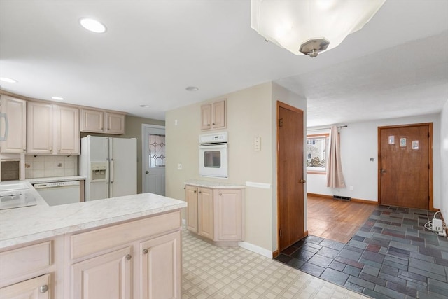 kitchen with backsplash, white appliances, and light brown cabinetry