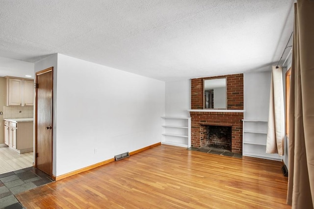 unfurnished living room featuring a brick fireplace, light hardwood / wood-style flooring, and a textured ceiling