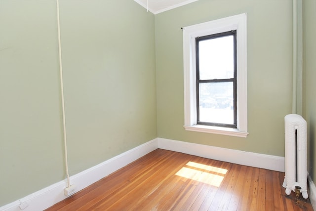 empty room with radiator heating unit, crown molding, and hardwood / wood-style flooring