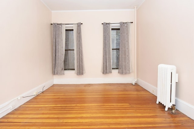 spare room with radiator heating unit, ornamental molding, and hardwood / wood-style flooring