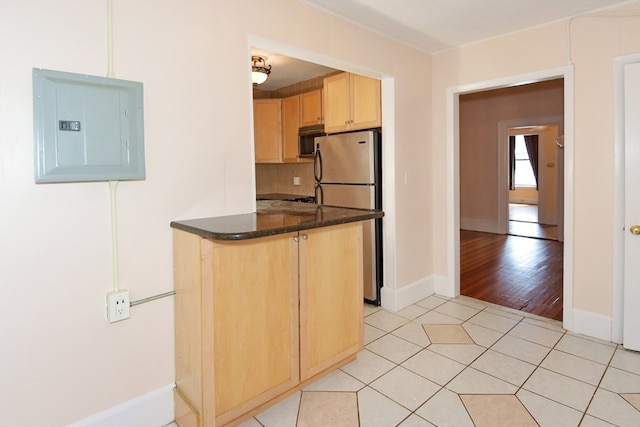 kitchen with tasteful backsplash, appliances with stainless steel finishes, light brown cabinetry, electric panel, and light hardwood / wood-style flooring