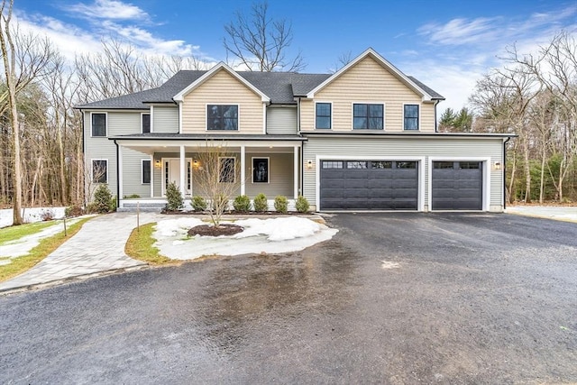 traditional-style home with covered porch, driveway, a shingled roof, and a garage