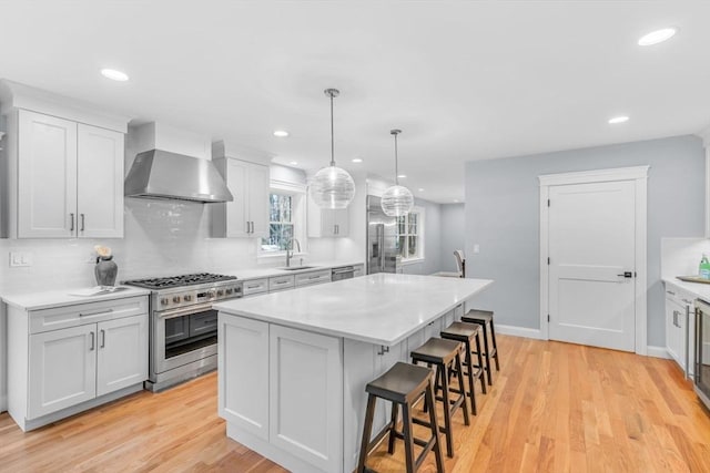 kitchen with a kitchen island, appliances with stainless steel finishes, wall chimney range hood, a kitchen bar, and a sink