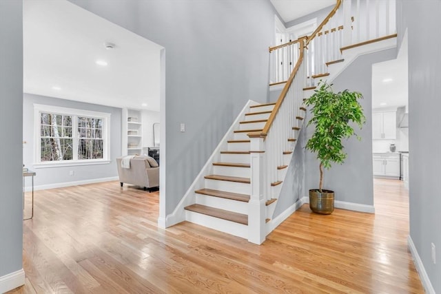 stairway featuring baseboards, wood finished floors, built in shelves, a fireplace, and recessed lighting