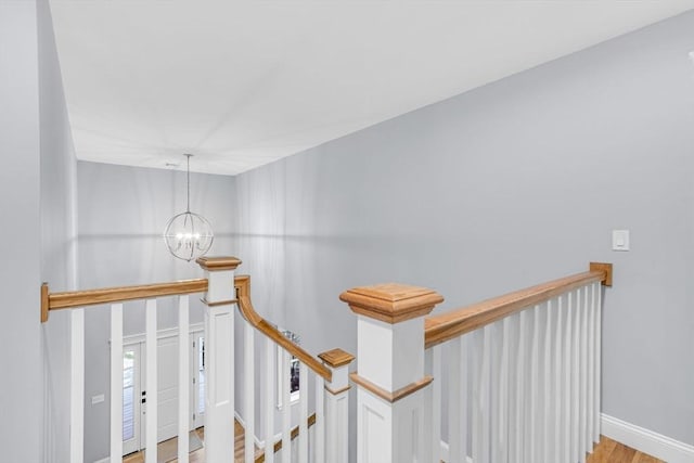 hall with an inviting chandelier, light wood-style flooring, baseboards, and an upstairs landing