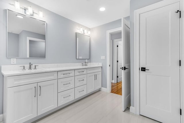 full bathroom with double vanity, wood finished floors, a sink, and baseboards