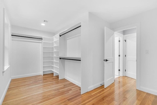 walk in closet with light wood finished floors, a barn door, and visible vents