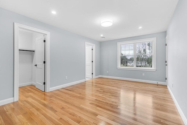 unfurnished bedroom featuring light wood-style floors, a spacious closet, and baseboards