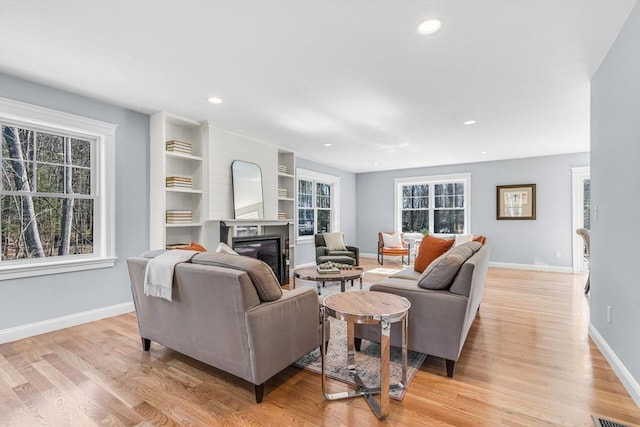 living room with light wood finished floors, a glass covered fireplace, recessed lighting, and baseboards