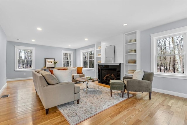 living room with baseboards, visible vents, light wood-style floors, a fireplace, and recessed lighting