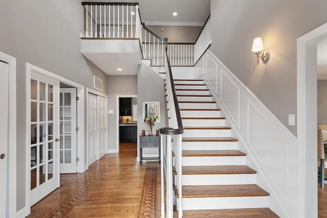 staircase with french doors, a towering ceiling, and hardwood / wood-style flooring