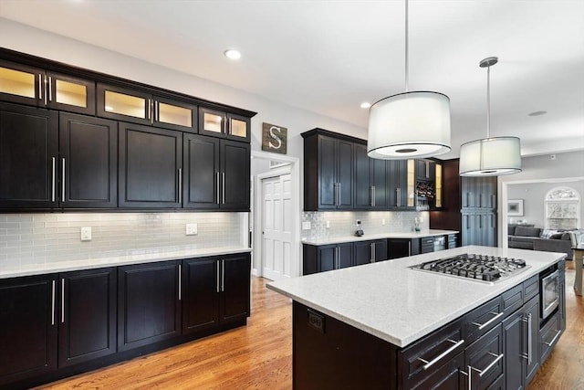 kitchen with appliances with stainless steel finishes, tasteful backsplash, pendant lighting, light hardwood / wood-style floors, and a kitchen island