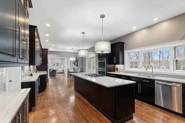 kitchen featuring backsplash, hanging light fixtures, hardwood / wood-style flooring, appliances with stainless steel finishes, and a kitchen island