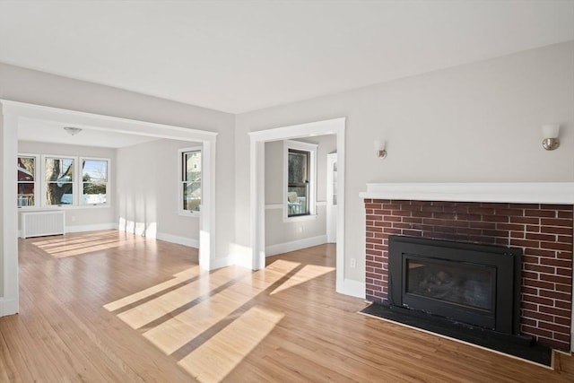 unfurnished living room featuring light wood-type flooring, radiator heating unit, and a fireplace