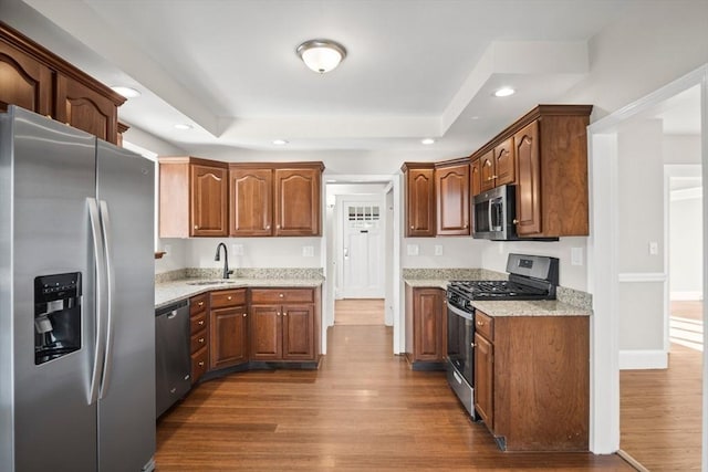 kitchen with appliances with stainless steel finishes, light stone counters, dark wood-type flooring, and sink