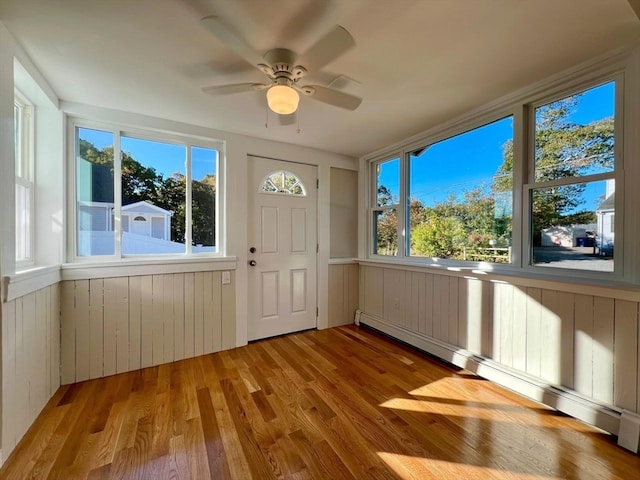 unfurnished sunroom with ceiling fan and a baseboard heating unit