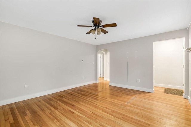 spare room featuring light wood-type flooring, arched walkways, ceiling fan, and baseboards