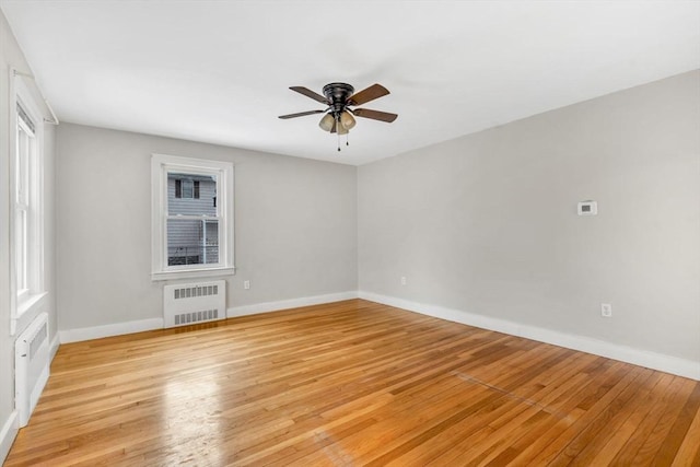 spare room with radiator, light wood-style flooring, baseboards, and a ceiling fan