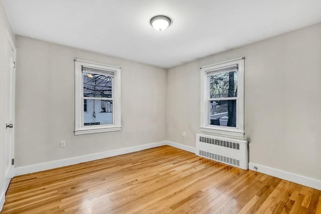 empty room featuring radiator heating unit, baseboards, and light wood-style flooring