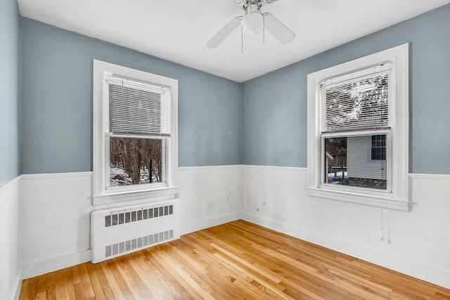 unfurnished room featuring a healthy amount of sunlight, a wainscoted wall, radiator heating unit, and wood-type flooring