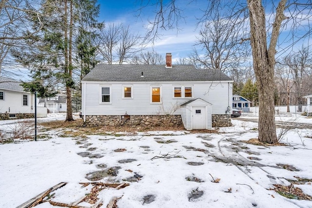 snow covered house featuring a shingled roof and a chimney