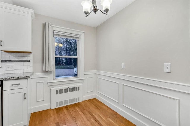 unfurnished dining area featuring a chandelier, light wood-type flooring, radiator, and a wainscoted wall