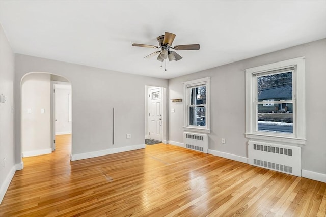 empty room with arched walkways, light wood-style floors, baseboards, and radiator