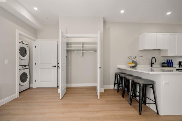 kitchen with stacked washer / dryer, a kitchen breakfast bar, light countertops, white cabinetry, and light wood finished floors