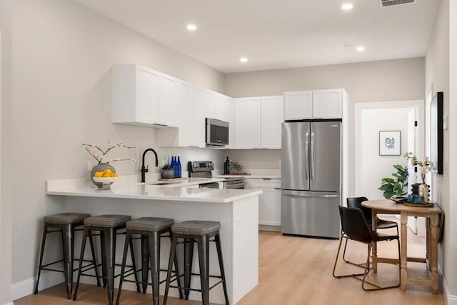 kitchen featuring appliances with stainless steel finishes, a sink, a peninsula, light countertops, and a kitchen bar