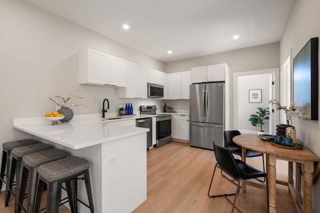 kitchen featuring stainless steel appliances, a sink, a peninsula, a kitchen bar, and light countertops