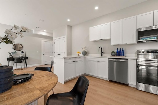 kitchen with stainless steel appliances, a sink, a peninsula, light countertops, and light wood-style flooring