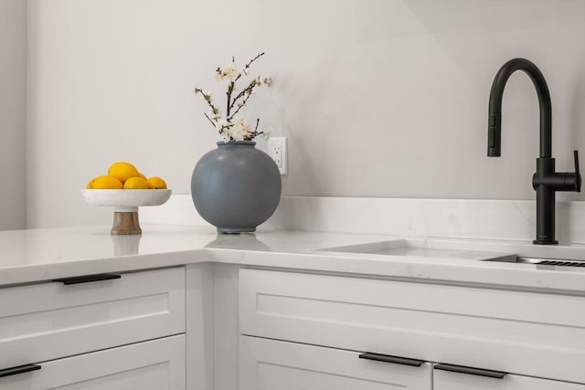 detailed view of a sink, white cabinets, and light stone countertops