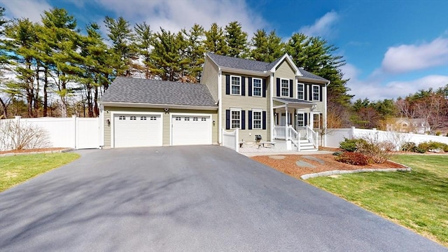 colonial house with a front lawn, aphalt driveway, covered porch, fence, and a garage