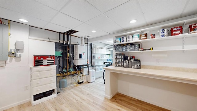 interior space featuring light wood finished floors, a drop ceiling, baseboards, recessed lighting, and water heater