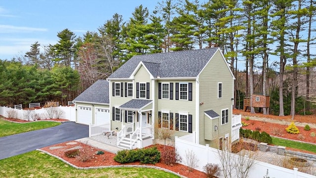 view of front facade with a shingled roof, fence, and aphalt driveway