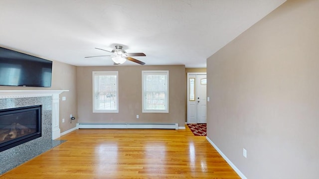unfurnished living room with a baseboard radiator, a high end fireplace, ceiling fan, and light wood-type flooring