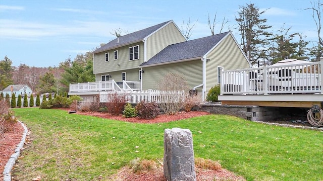 rear view of property featuring a lawn, roof with shingles, and a deck