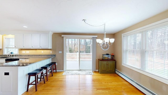 kitchen featuring a baseboard heating unit, a sink, white cabinetry, a notable chandelier, and a breakfast bar area