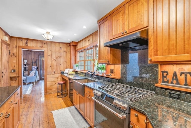 kitchen with under cabinet range hood, a sink, light wood-type flooring, brown cabinets, and gas stove