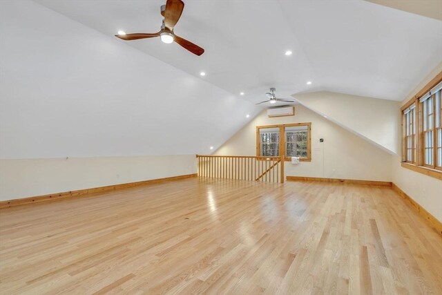 additional living space with light wood finished floors, baseboards, a wall mounted air conditioner, vaulted ceiling, and recessed lighting