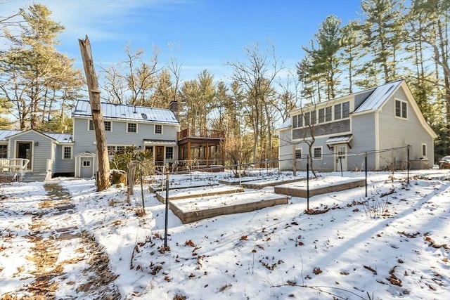 snow covered house featuring metal roof, an outdoor structure, fence, a sunroom, and a standing seam roof