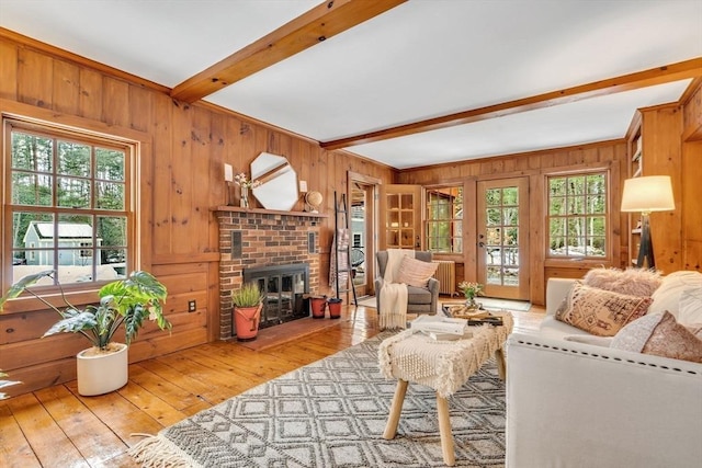 living room featuring a fireplace, radiator, light wood-style floors, wooden walls, and beamed ceiling