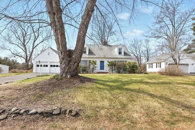 cape cod-style house featuring a front lawn, aphalt driveway, a chimney, and a detached garage