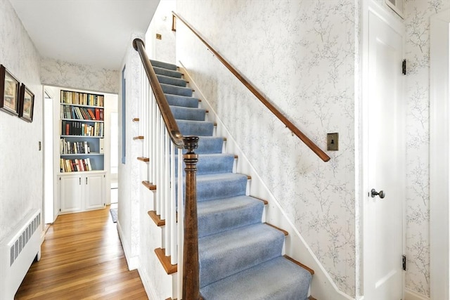 staircase with wallpapered walls, wood finished floors, and radiator
