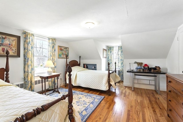 bedroom with baseboards, vaulted ceiling, radiator heating unit, and hardwood / wood-style flooring