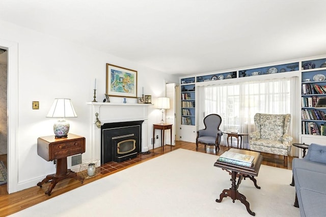 living area featuring baseboards, a wood stove, wood finished floors, and built in shelves