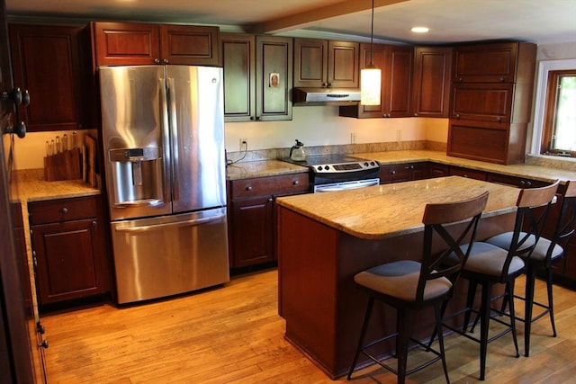 kitchen featuring under cabinet range hood, a kitchen bar, light wood finished floors, and stainless steel appliances